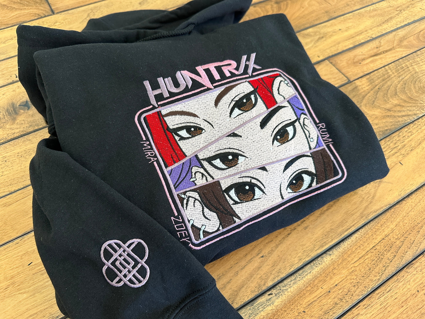 Black hoodie with 'HUNTRIX' design on a wooden floor