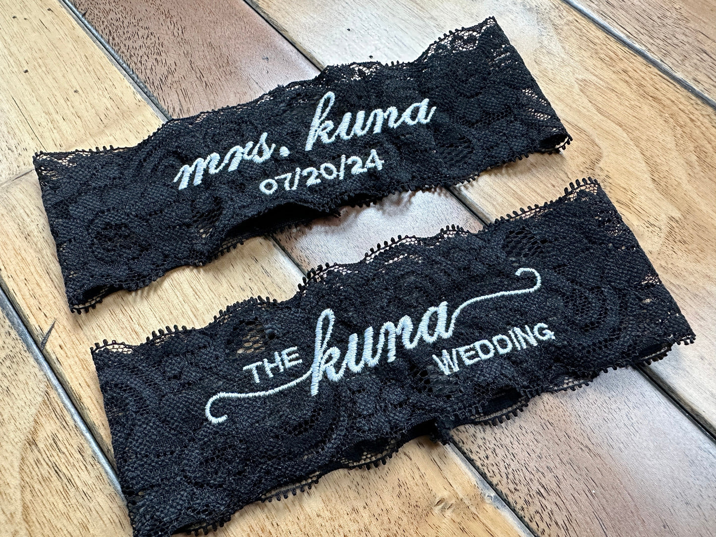 A set of custom embroidered wedding garter in black lace.  The personalization includes the bride's new last name for the keepsake garter.  The toss garter also has the family's name.