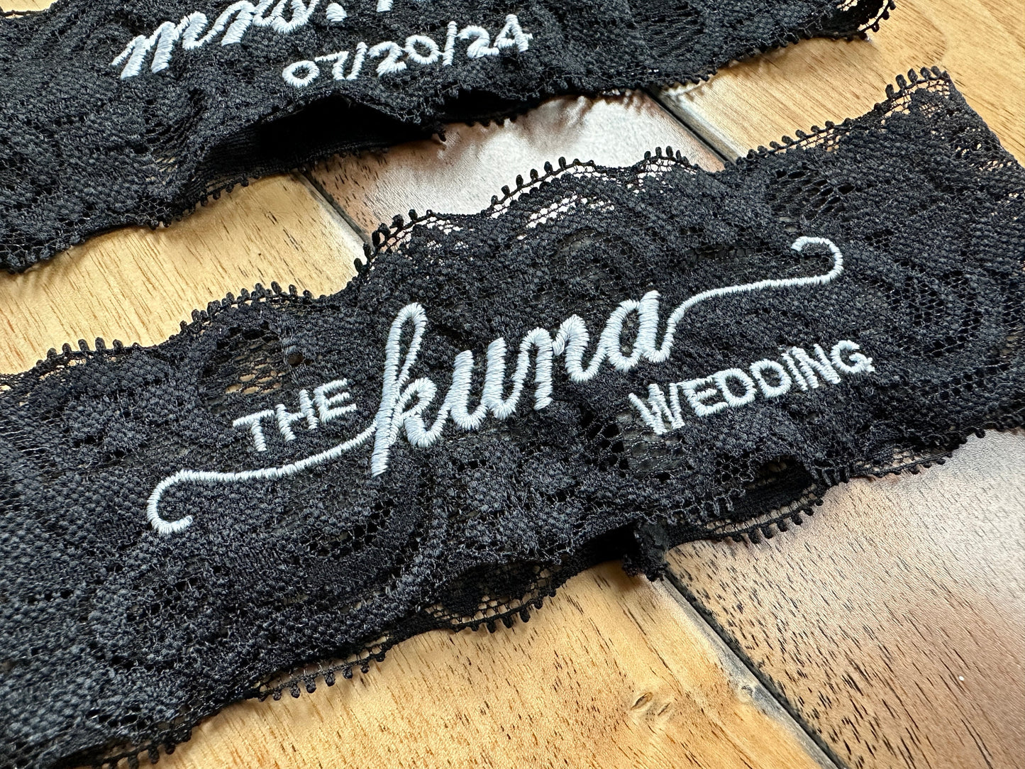Black lace bridal garter with 'The Kuna Wedding' text on a wooden surface