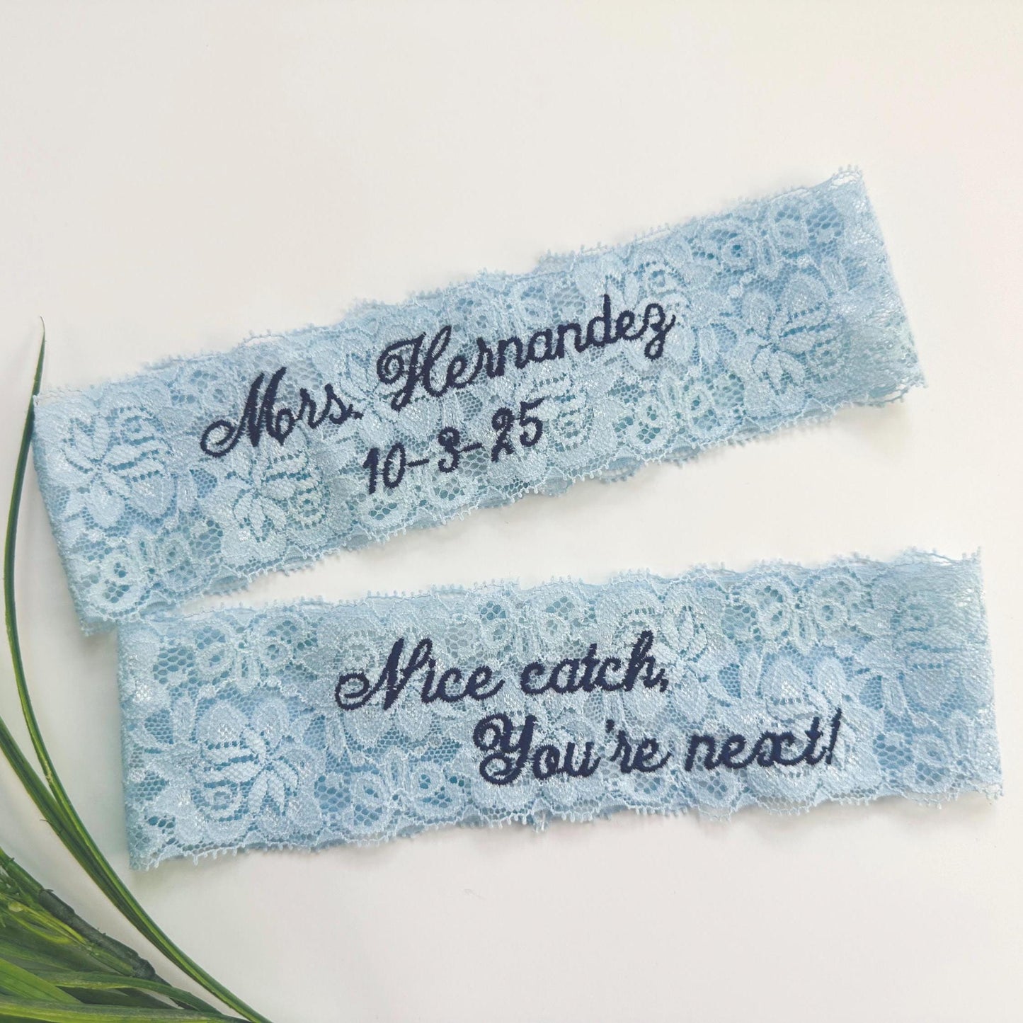 something blue wedding garter in light blue lace with embroidery details of her new last name and the wedding date.  The matching toss garter with embroidery that says "nice catch, you're next". The lace has a classic floral pattern.